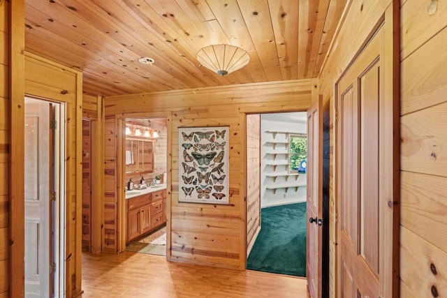 hallway featuring light wood-type flooring, wood ceiling, and wooden walls