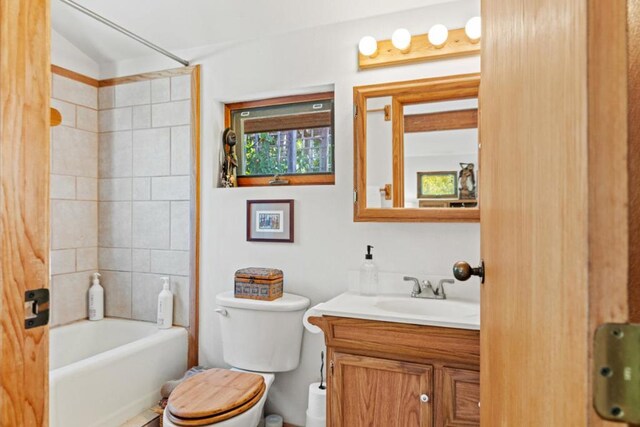 full bathroom featuring tiled shower / bath, vanity, toilet, and lofted ceiling