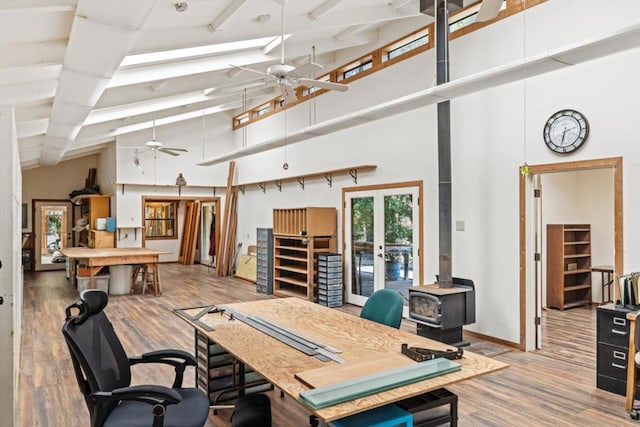 office space featuring high vaulted ceiling, beamed ceiling, a wood stove, ceiling fan, and light wood-type flooring