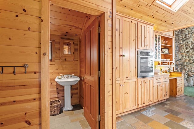 kitchen featuring wooden walls, a skylight, stainless steel oven, light brown cabinets, and wooden ceiling