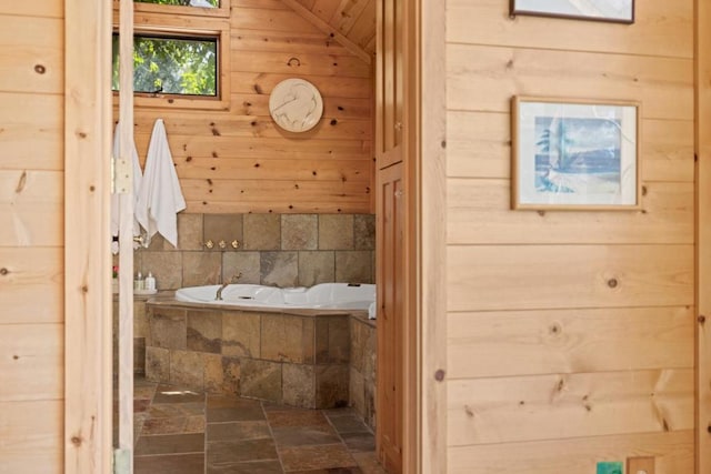 bathroom with lofted ceiling, wooden walls, and tiled bath