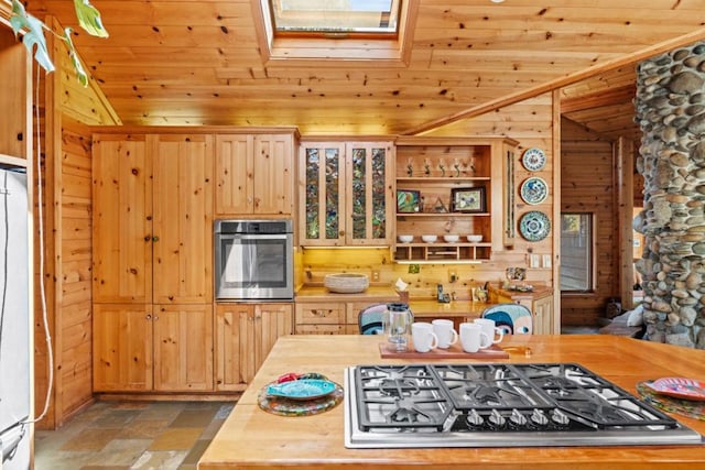 kitchen featuring wood ceiling, appliances with stainless steel finishes, butcher block counters, wooden walls, and lofted ceiling with skylight