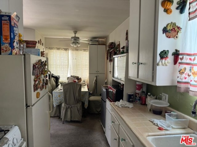 kitchen with white appliances, ceiling fan, sink, tile countertops, and white cabinets