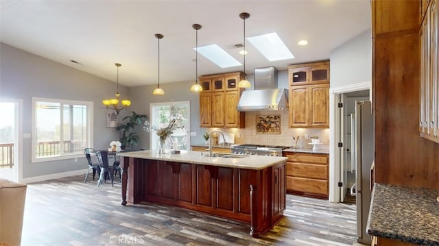 kitchen featuring plenty of natural light, wall chimney range hood, sink, and an island with sink