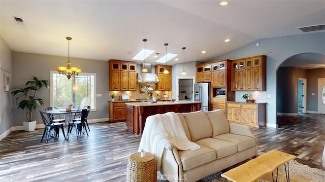 living room featuring dark wood-type flooring, vaulted ceiling with skylight, and a chandelier