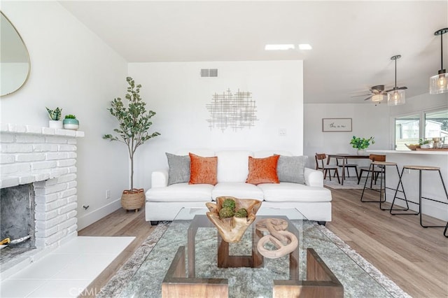 living room featuring ceiling fan, a fireplace, and light hardwood / wood-style flooring