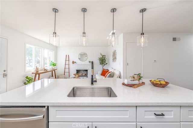 kitchen with white cabinetry, sink, stainless steel dishwasher, pendant lighting, and a fireplace