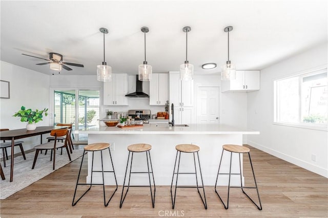 kitchen featuring wall chimney exhaust hood, an island with sink, white cabinets, and light hardwood / wood-style floors