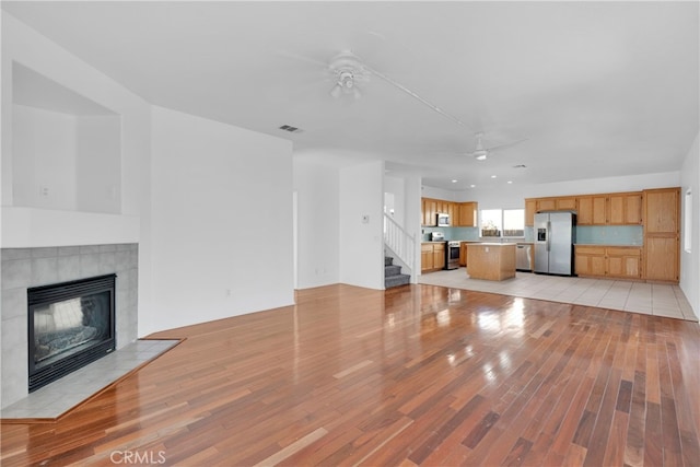 unfurnished living room with ceiling fan, light wood-type flooring, and a fireplace