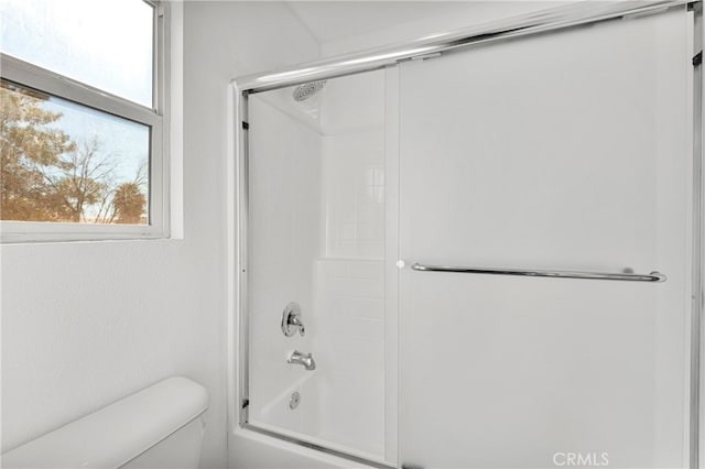 bathroom with toilet and shower / bath combination with glass door