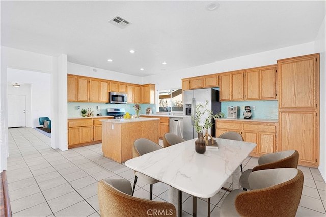 kitchen with a breakfast bar area, a kitchen island, light tile patterned floors, and appliances with stainless steel finishes