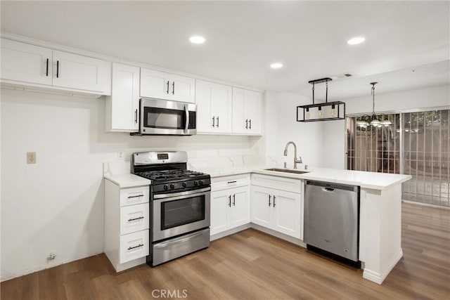 kitchen with kitchen peninsula, light wood-type flooring, stainless steel appliances, white cabinetry, and hanging light fixtures