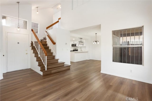 unfurnished living room with a chandelier, dark hardwood / wood-style flooring, high vaulted ceiling, and sink