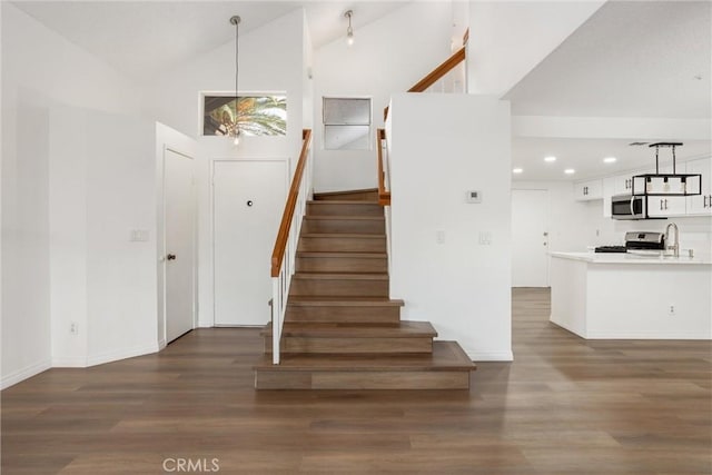 stairs with wood-type flooring, sink, and high vaulted ceiling