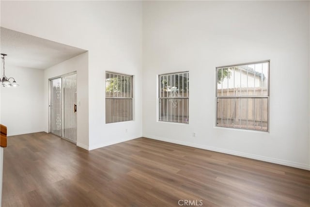 empty room with a towering ceiling, dark wood-type flooring, and an inviting chandelier