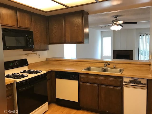 kitchen with kitchen peninsula, dark brown cabinets, white appliances, sink, and light hardwood / wood-style flooring