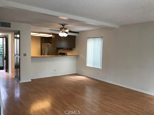 unfurnished living room featuring a textured ceiling, dark hardwood / wood-style flooring, ceiling fan, and beam ceiling