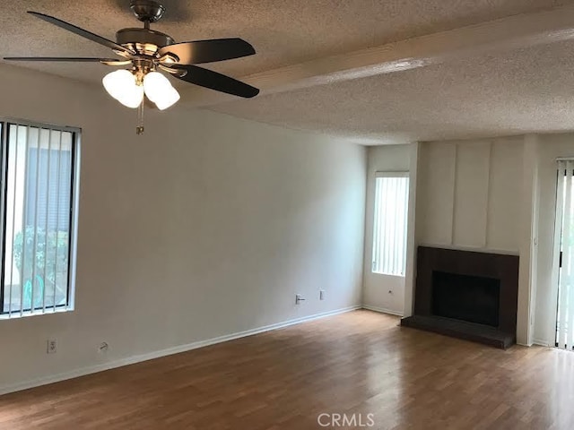 unfurnished living room with beam ceiling, a textured ceiling, hardwood / wood-style flooring, and ceiling fan