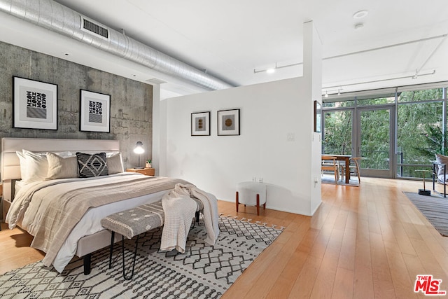 bedroom with a wall of windows and light hardwood / wood-style flooring