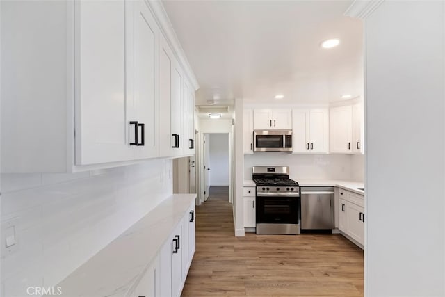 kitchen with white cabinets, tasteful backsplash, light wood-type flooring, stainless steel appliances, and light stone counters