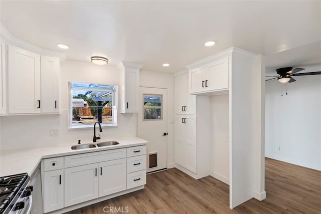 kitchen featuring dark wood-type flooring, stainless steel gas range oven, sink, and white cabinets