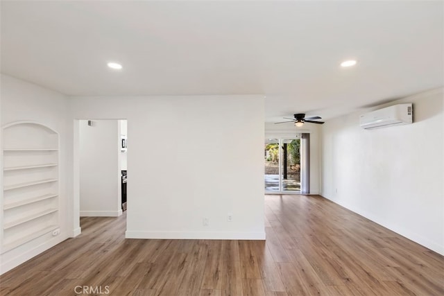 unfurnished room featuring a wall mounted AC, hardwood / wood-style flooring, built in features, and ceiling fan