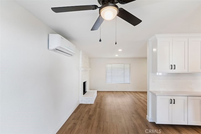 unfurnished living room featuring a wall mounted air conditioner, ceiling fan, wood-type flooring, and a brick fireplace