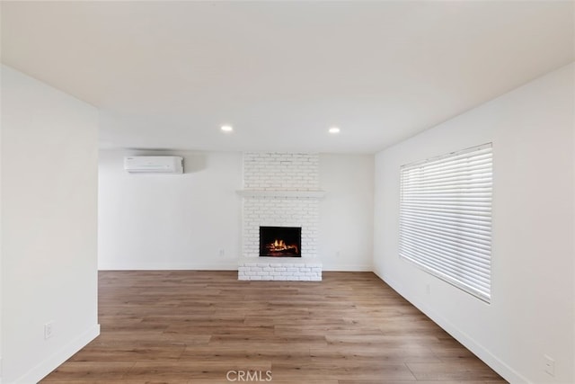 unfurnished living room with a wall unit AC, a fireplace, and light wood-type flooring