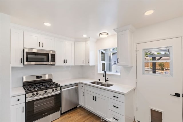 kitchen with sink, decorative columns, white cabinetry, appliances with stainless steel finishes, and light hardwood / wood-style floors