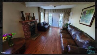 living room featuring beam ceiling, a brick fireplace, and wood-type flooring