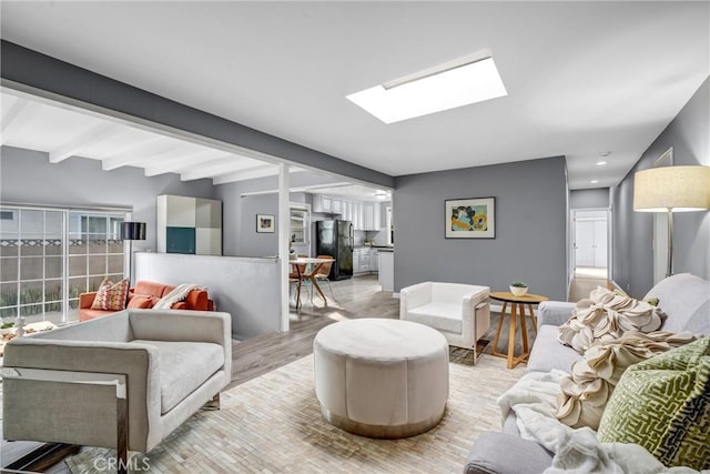 living room with a skylight, beamed ceiling, and light hardwood / wood-style floors