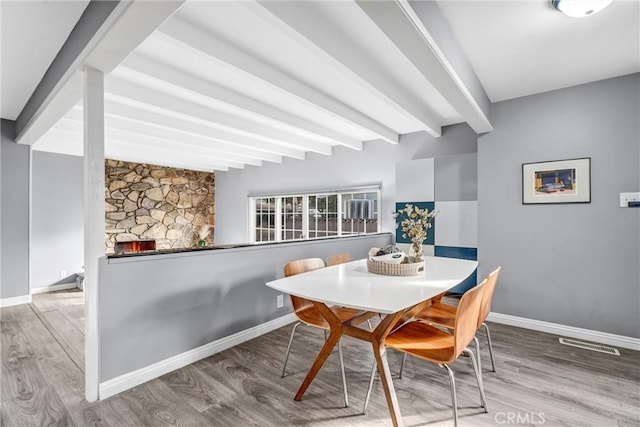 dining room featuring a fireplace, hardwood / wood-style floors, and beam ceiling