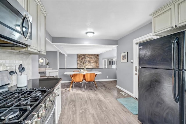 kitchen featuring backsplash, cream cabinetry, light hardwood / wood-style floors, and appliances with stainless steel finishes