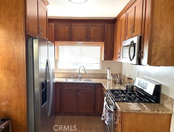 kitchen with light stone counters, sink, stainless steel appliances, and dark hardwood / wood-style floors