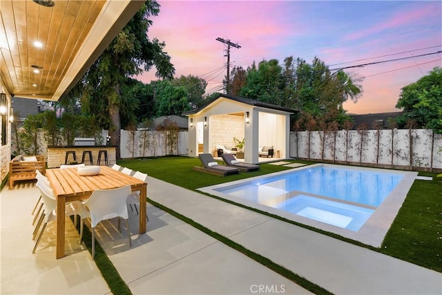 pool at dusk with an in ground hot tub, a patio, an outdoor structure, a lawn, and an outdoor hangout area