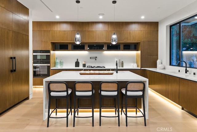 kitchen with a kitchen bar, an island with sink, decorative light fixtures, double oven, and sink