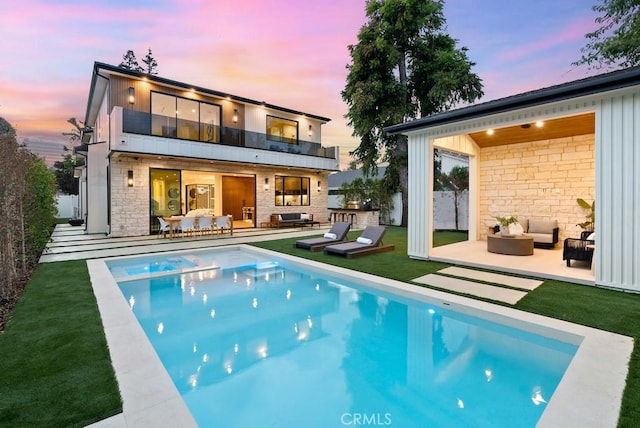 back house at dusk with a balcony, outdoor lounge area, and a patio