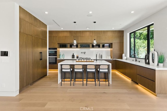 kitchen featuring pendant lighting, a kitchen island, a breakfast bar area, light hardwood / wood-style flooring, and multiple ovens