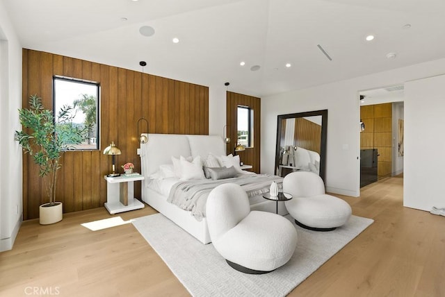 bedroom featuring multiple windows, light hardwood / wood-style flooring, and wood walls