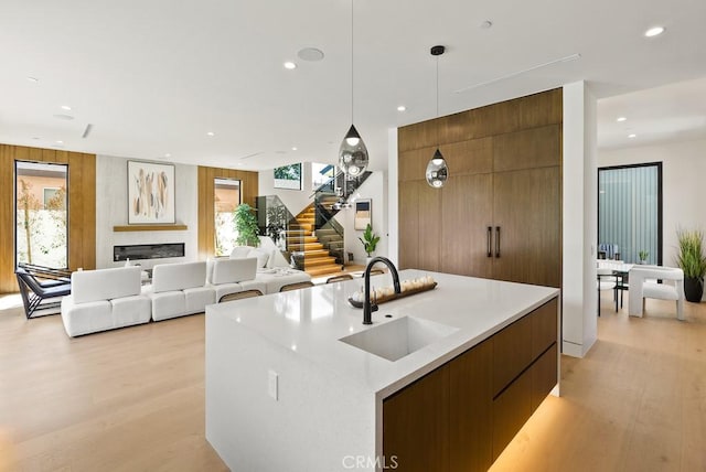 kitchen featuring wood walls, a center island with sink, light wood-type flooring, hanging light fixtures, and sink