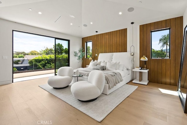 bedroom with light wood-type flooring, wooden walls, and high vaulted ceiling