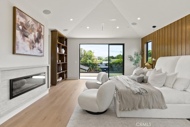 bedroom with light hardwood / wood-style floors, access to exterior, high vaulted ceiling, and wooden walls