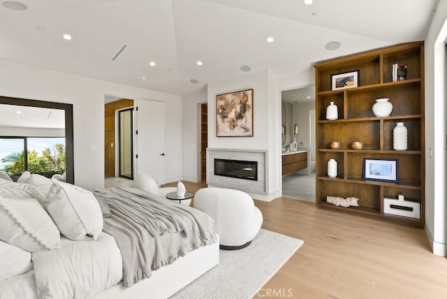 bedroom featuring connected bathroom, light hardwood / wood-style flooring, and vaulted ceiling