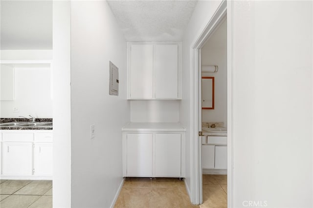 hallway with a textured ceiling, electric panel, sink, and light tile patterned floors