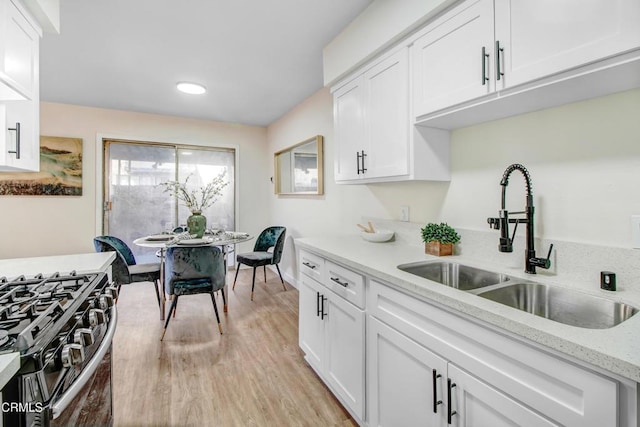 kitchen with light stone countertops, sink, stainless steel gas range oven, light hardwood / wood-style flooring, and white cabinets