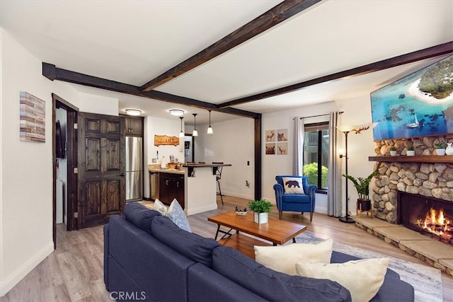 living room featuring beamed ceiling, light hardwood / wood-style flooring, and a stone fireplace