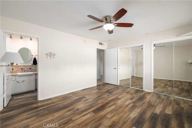 unfurnished bedroom with sink, dark hardwood / wood-style floors, ceiling fan, connected bathroom, and multiple closets