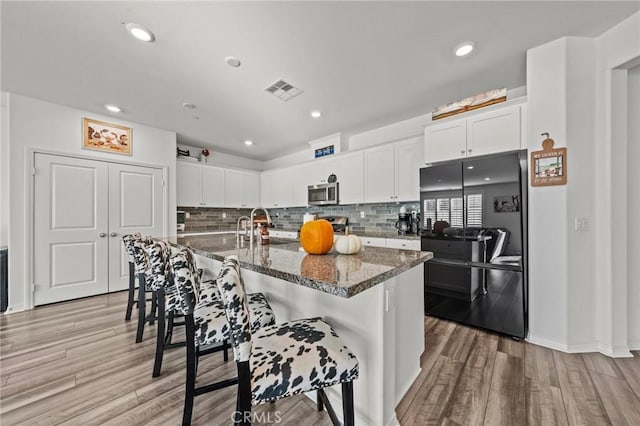 kitchen featuring light wood finished floors, stainless steel microwave, tasteful backsplash, and black refrigerator