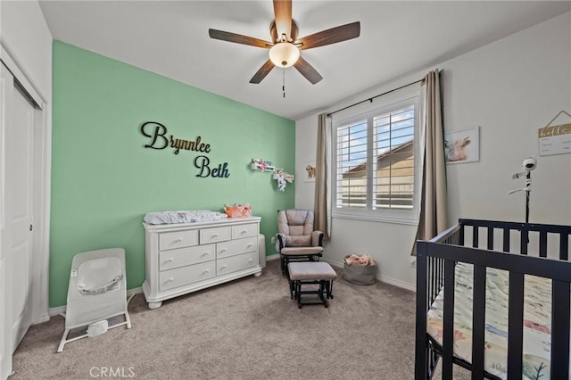 carpeted bedroom featuring a nursery area, baseboards, a closet, and ceiling fan