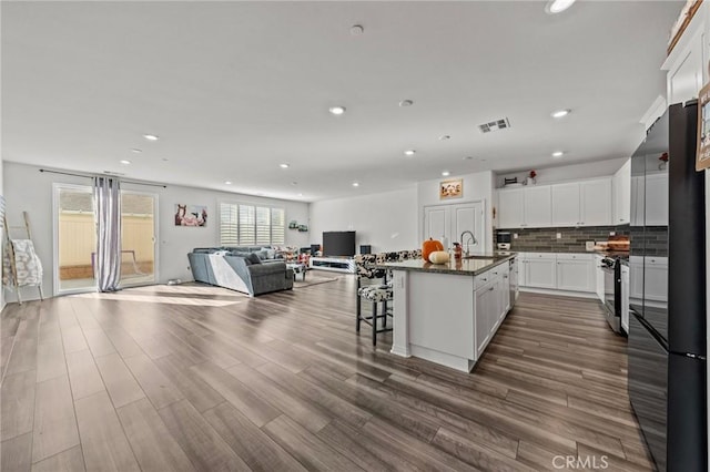 kitchen featuring backsplash, open floor plan, range with gas stovetop, white cabinetry, and a sink